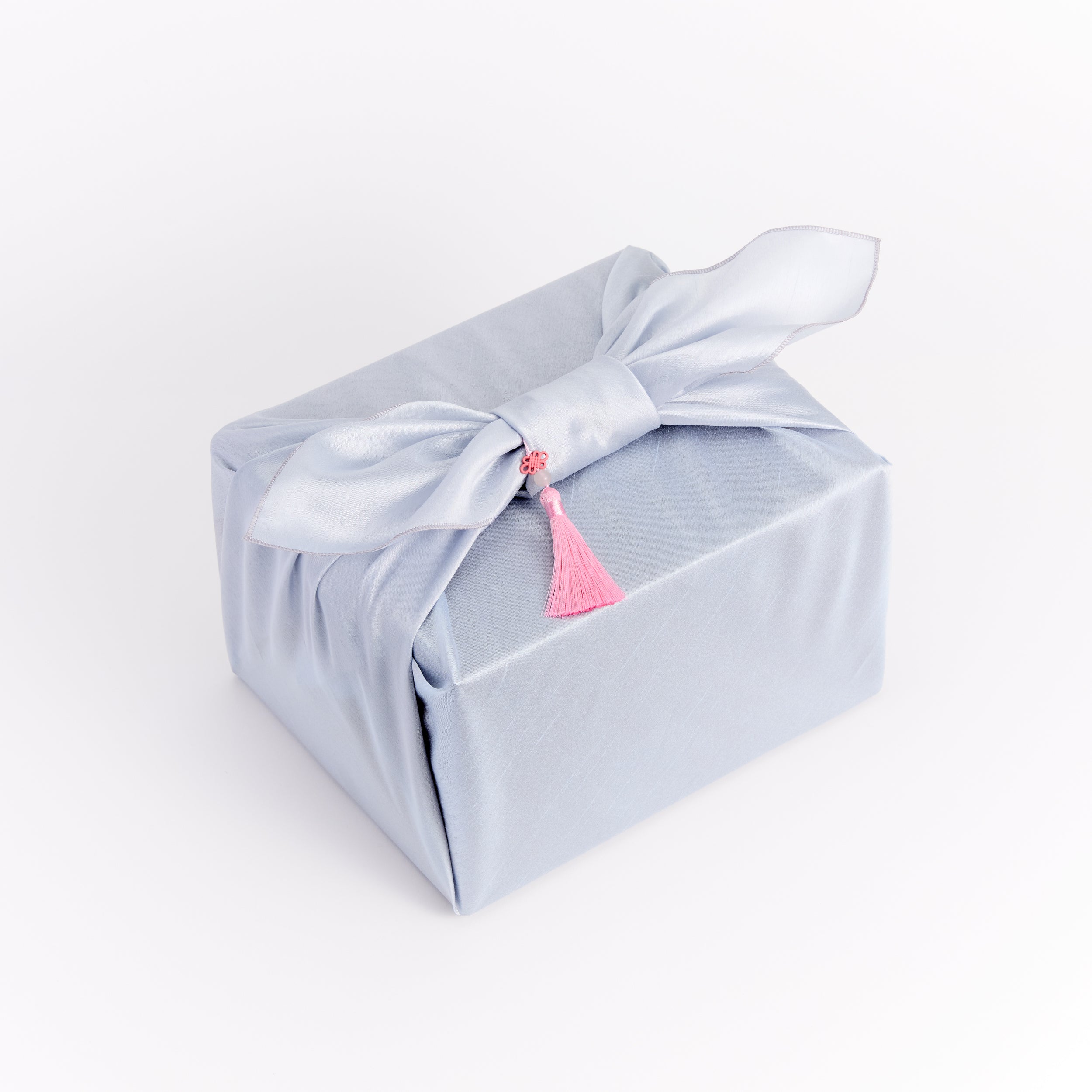 Gift box wrapped in light blue fabric with a pink tassel on a white background