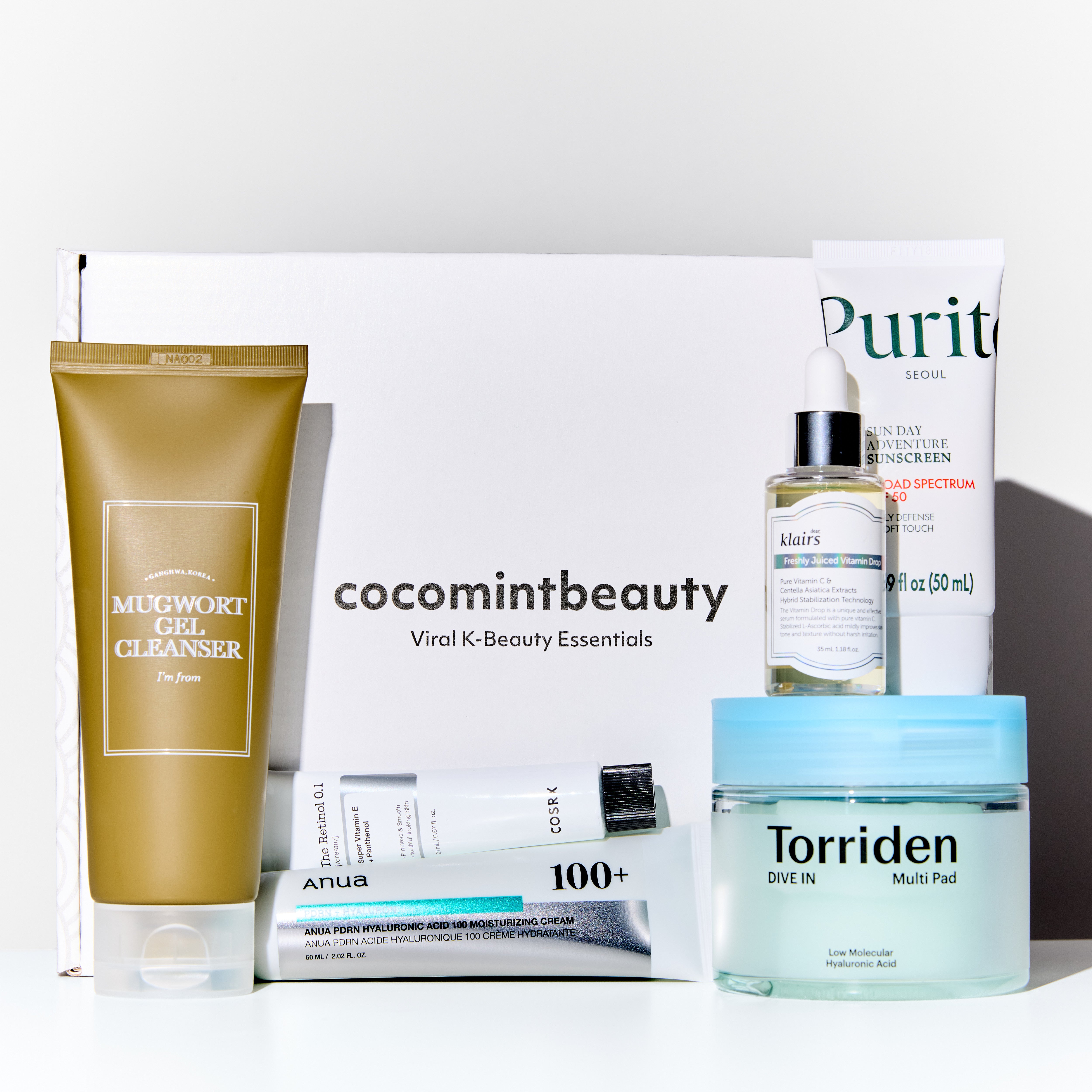 Collection of skincare products including a gold tube, white box, and blue jar on a white background.